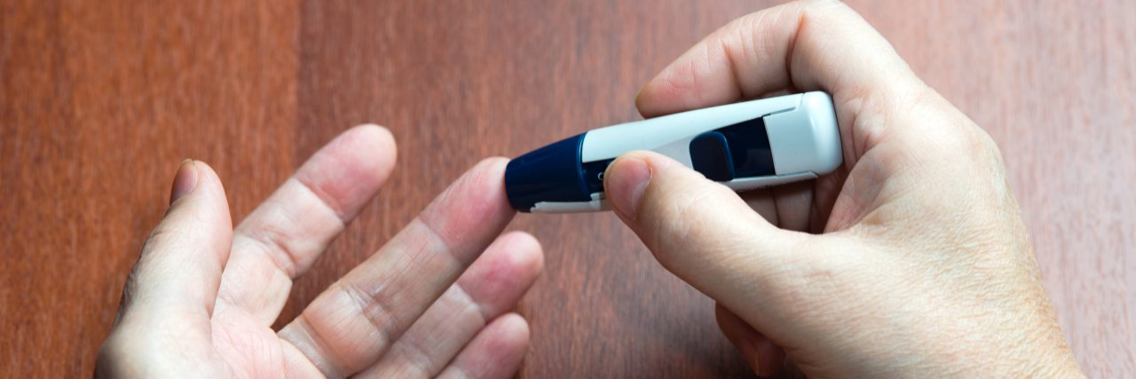 18 People Living With Type 1 Diabetes Explain What It's Like Hands holding blood glucose monitor to prick finger to measure levels