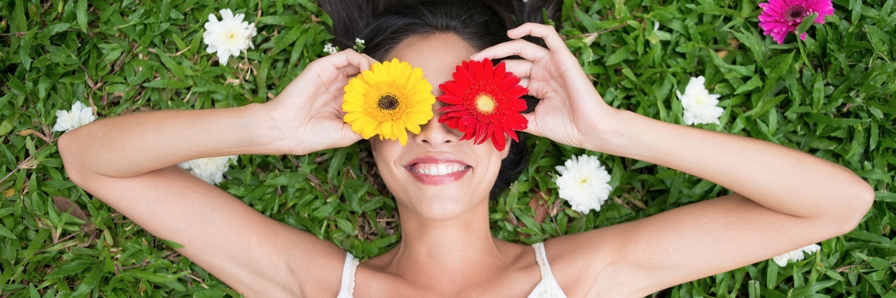 Ulcerative Colitis: The Power of Having Choices When You're Sick woman in white dress laying on the grass and holding red and yellow flowers over her eyes