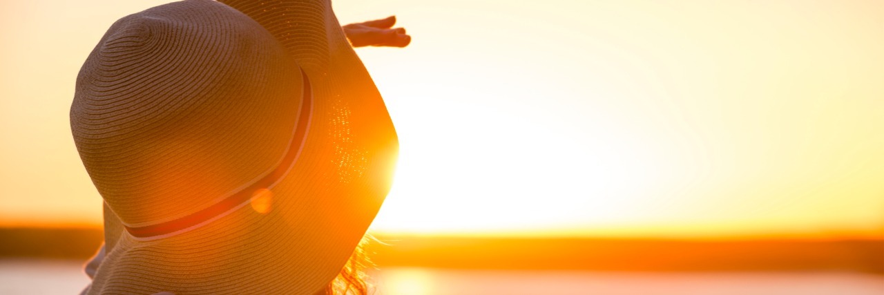 What It's Like Being Single With a Chronic Illness Young and beautiful woman wearing a hat in sunset light looking far away. Photo from behind