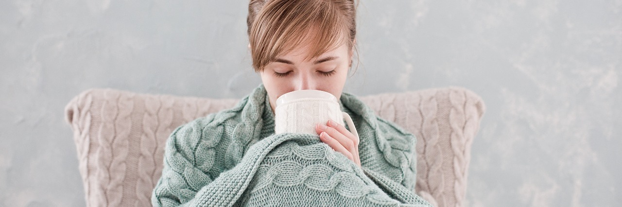 Self-Care Essentials for Bad Days With Illness woman wrapped in blanket and drinking out of mug