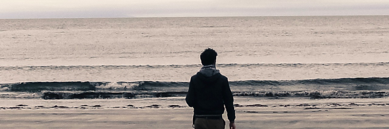 Grief Doesn't Have a Timeline Picture of man from behind walking on a beach on an overcast day