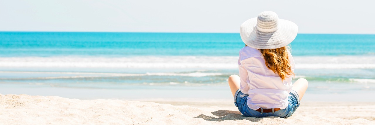 young woman sitting on the beach in white hat at sunny day