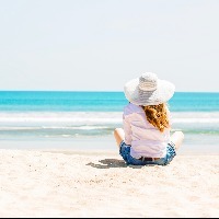 young woman sitting on the beach in white hat at sunny day