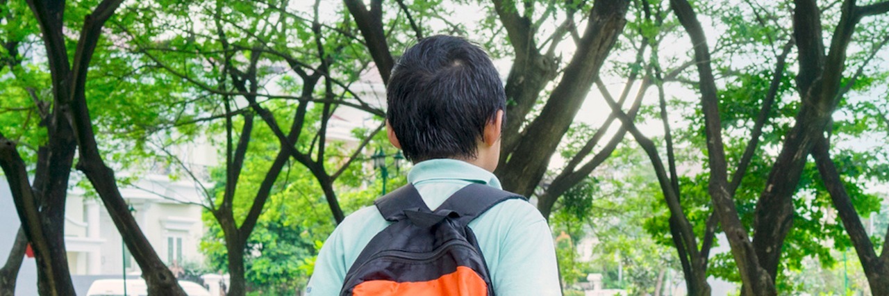 Boy wearing backpack, walking near grass and trees