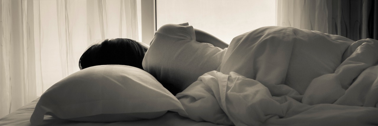 Self-Care: How to Know When to Rest or Push Through Fatigue Young woman lying in bed, looking towards through the window - black and white photo.