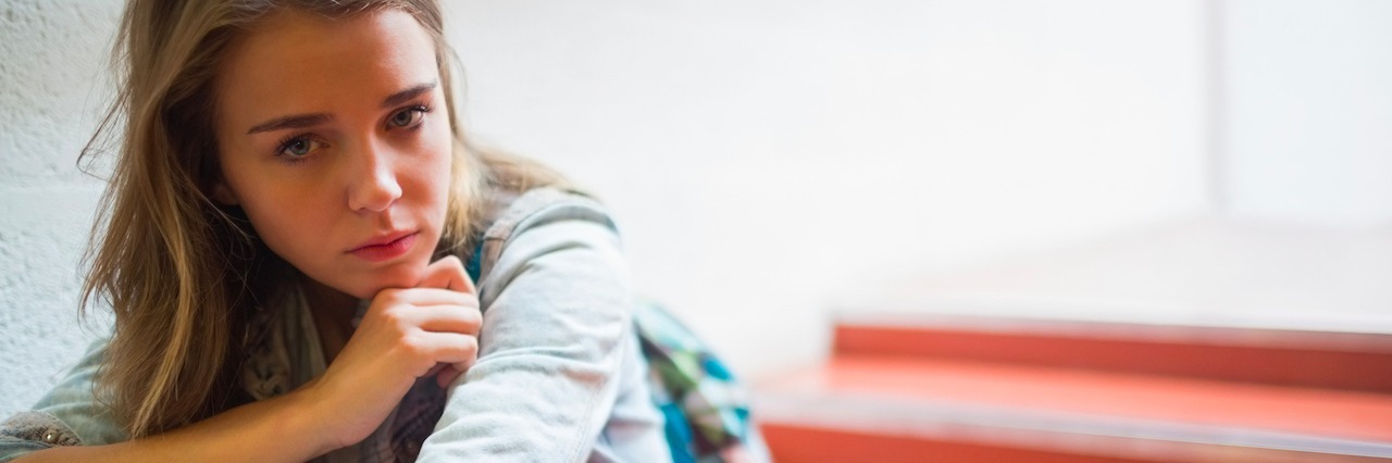 Tips for Navigating College With an Anxiety Disorder a sad student holding books sitting on a staircase