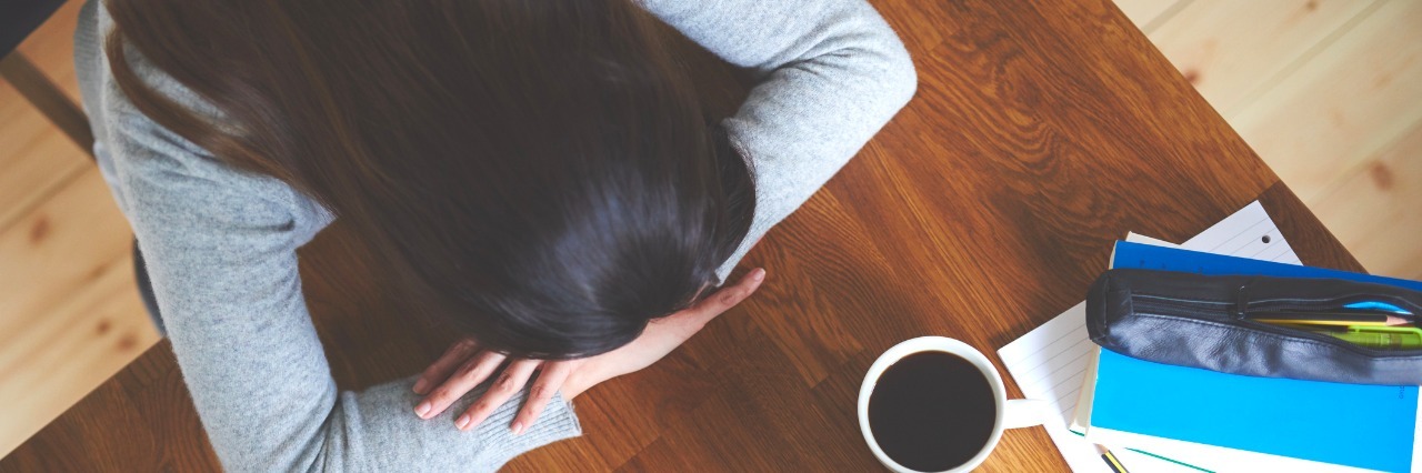 How to Respond to 4 Challenges of Having Weak Immune System View down of woman sitting at table in home office with head resting on hands.