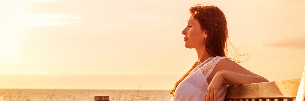 Maintaining Purpose With Chronic Illness woman relaxing on a bench next to the ocean at sunset
