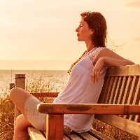woman relaxing on a bench next to the ocean at sunset