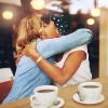 Two affectionate girl friends embracing as they sit in a coffee shop enjoying a cup of coffee together