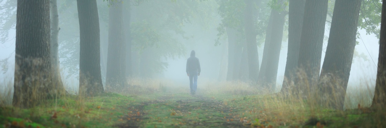 Anonymous man in hoodie walking alone in a lane on a foggy, autumn morning.
