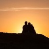 Silhouette of two people sitting on a rock at sunset
