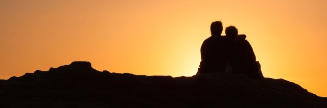 Silhouette of two people sitting on a rock at sunset