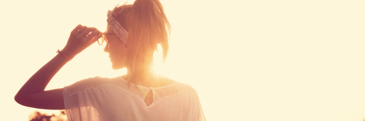Appreciating Good and Bad Moments With Chronic Illness woman in white shirt adjusting her glasses and looking at the sun