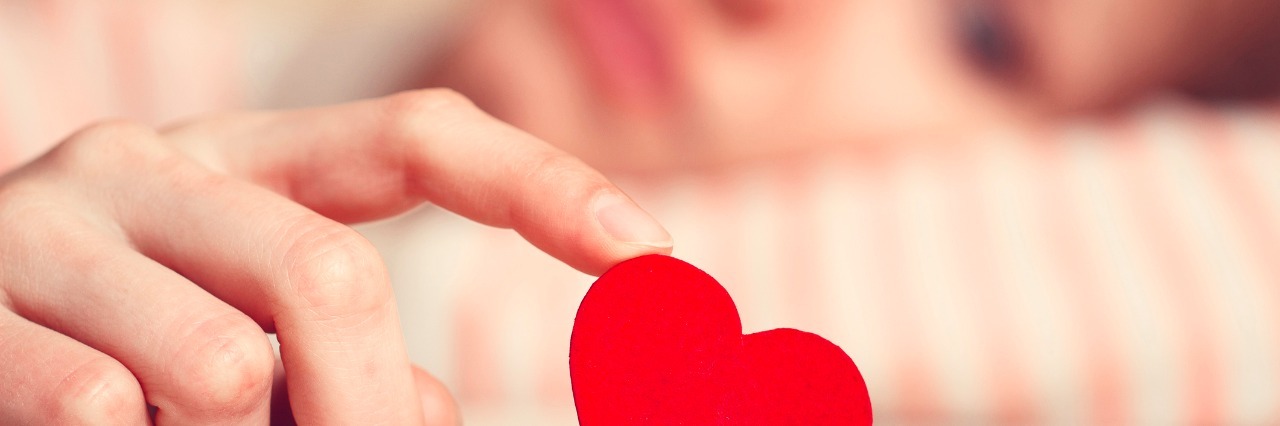 girl is holding heart symbol by her finger and looking at it