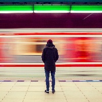 Lonely young man shot from behind at subway station with blurry moving train in background
