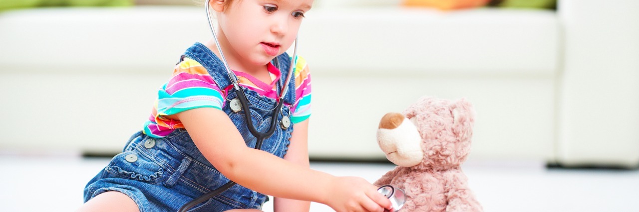 Child holding stethoscope to teddy bear's chest in home living room