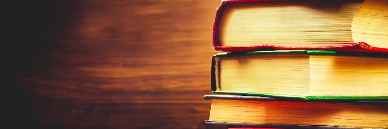 Why I Thrive on Challenge as an Autistic Person stack of books on a wooden table with a wood background