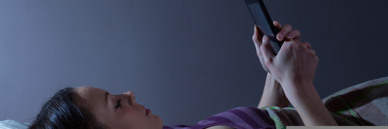 Helpful Apps for People with Chronic Pain woman lying in bed looking at smartphone