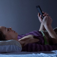woman lying in bed looking at smartphone