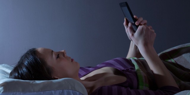 woman lying in bed looking at smartphone