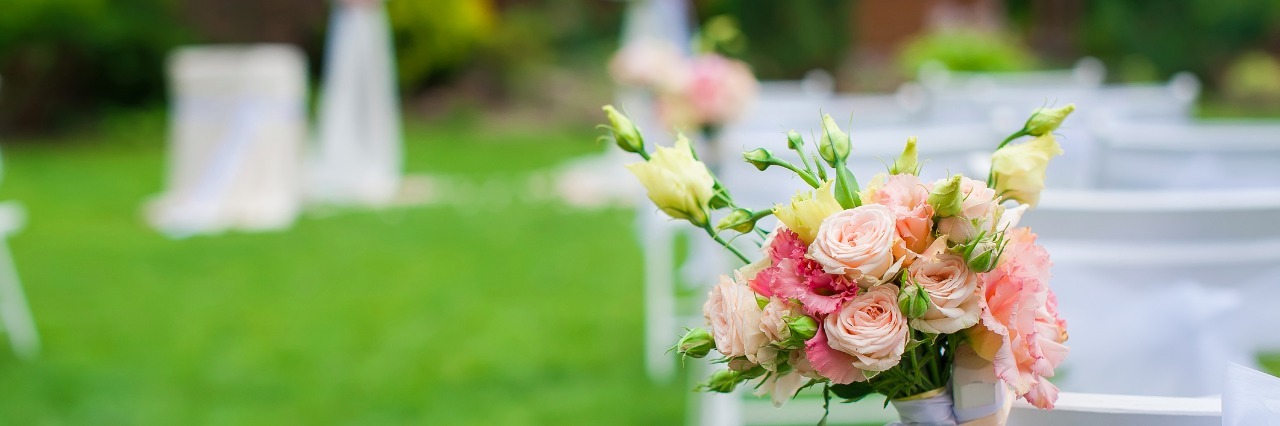How to Prepare for a Wedding When You Have Anxiety White chair standing on a green glade, prepared for the wedding ceremony. The chair is decorated with a bouquet of flowers. The background is blurred.