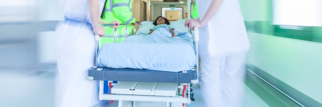A motion blurred photograph of a child patient on stretcher or gurney being pushed at speed through a hospital corridor by doctors & nurses to an emergency room
