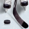 Close-up of hockey player's skates on ice with hockey stick in front of hockey puck