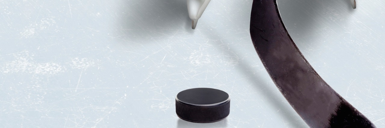Close-up of hockey player's skates on ice with hockey stick in front of hockey puck