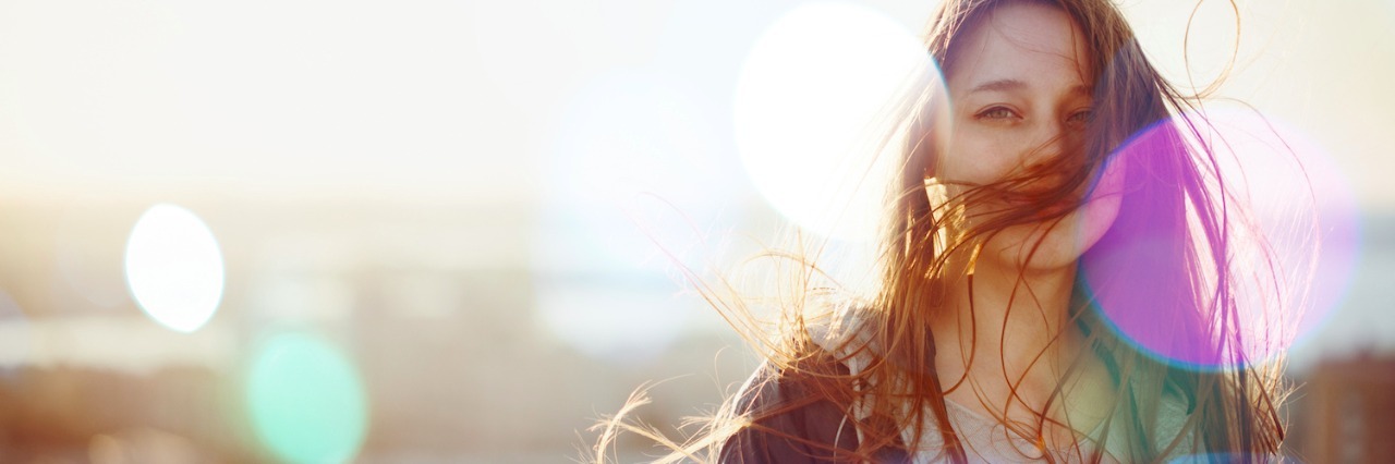 How I Think as an Autistic Person Woman looking at camera, standing in sunset light with wind blowing hair in front of face
