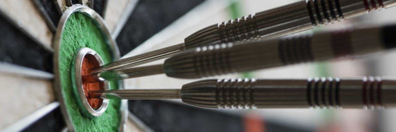 Closeup view of silhouette of three darts sticking in a professional sisal dartboard. All three darts hit the inner bull / bull's eye / mark.