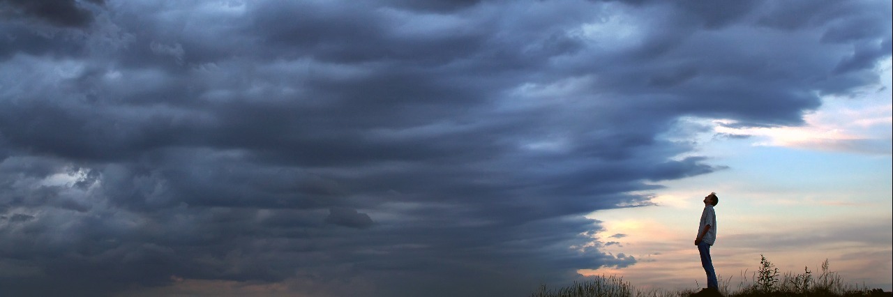 Difficulties of Living With Chronic Pain man standing in a field and facing a storm