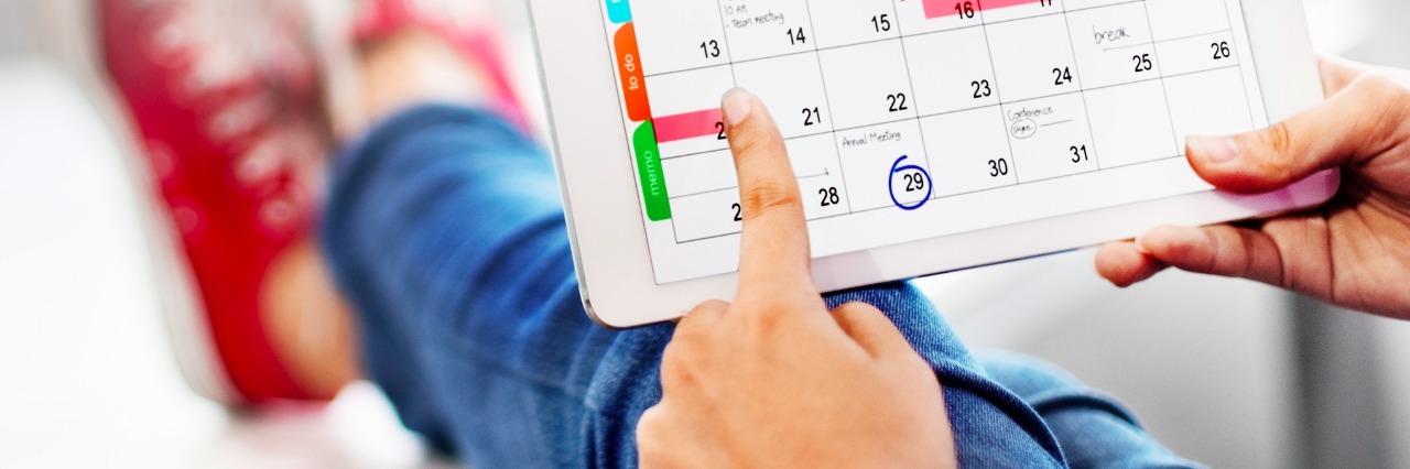 Tips For Sticking to a Schedule When You Have Fibromyalgia woman sitting on couch with feet up looking at calendar on tablet