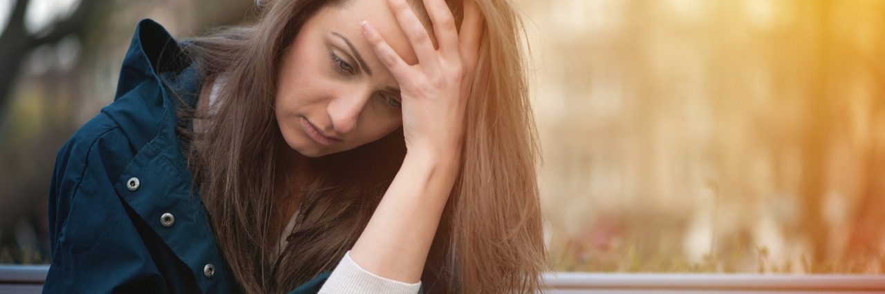 Crohn's Disease: Making Sacrifices for Your Health woman sitting on a park bench and looking at her phone sadly