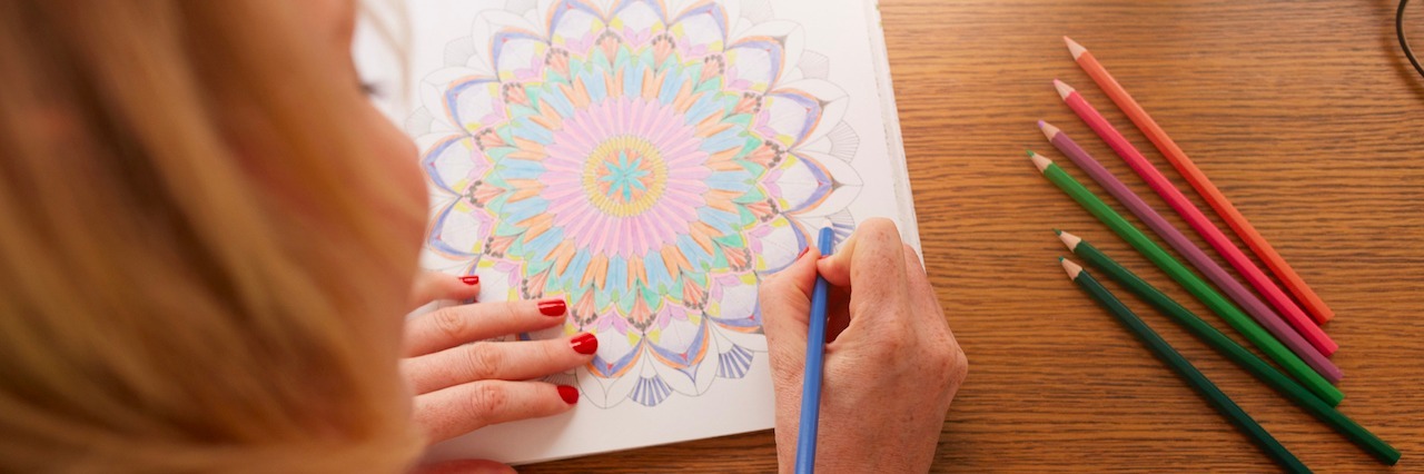 Overhead view of woman drawing in adult coloring book with color pencils.