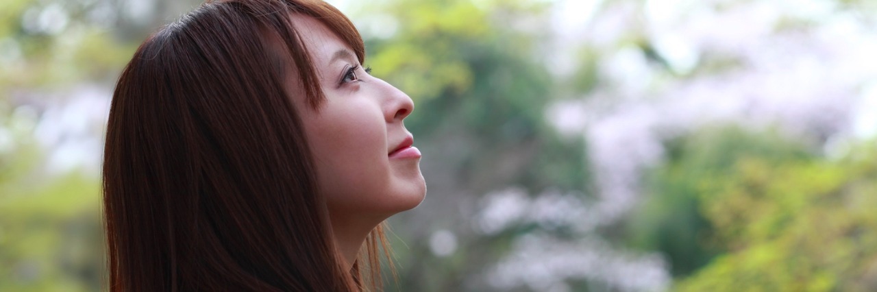 Profile of woman with gaze directed up, with trees in the background