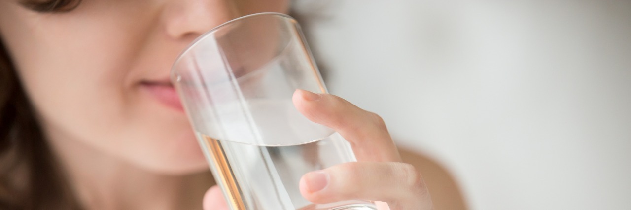 Easy Self Care Tips for When You Are Depressed Happy beautiful young woman drinking water. Smiling caucasian female model holding transparent glass in her hand. Closeup. Focus on the arm
