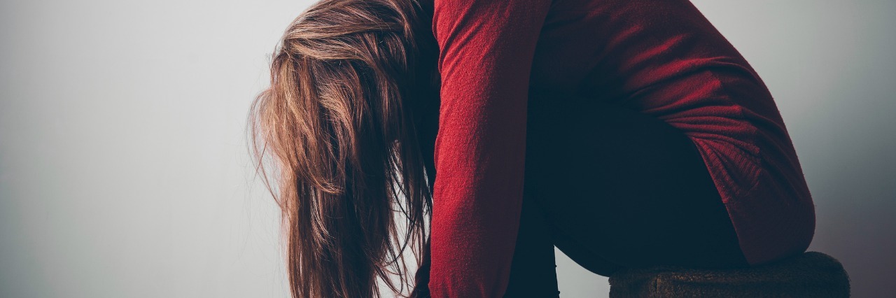 Why Being Told to 'Get Well Soon' Can Be Hurtful to Hear A woman sitting alone on stool hugging her knees