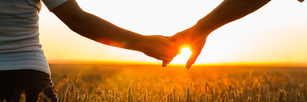 Young couple holding hands in the wheat field on sunny summer day.