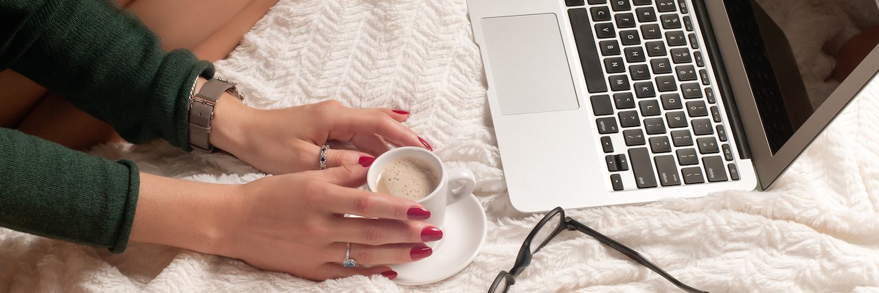 A woman holding a cup of tea sitting on front of her laptop