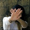 woman standing in front of a stone wall and holding her hands up to block her face