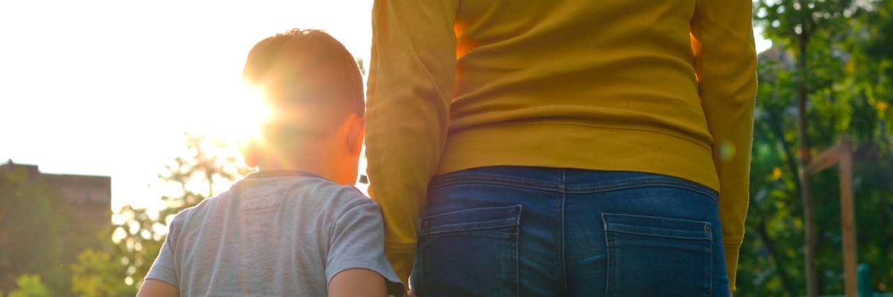 The Realities of Parenting With Chronic Pain Child holding hands with parent in nature at sunset.