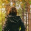 Woman wearing jacket, walking near trees in park in daytime