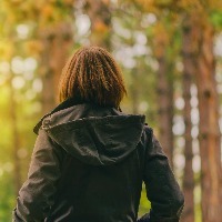 Woman wearing jacket, walking near trees in park in daytime