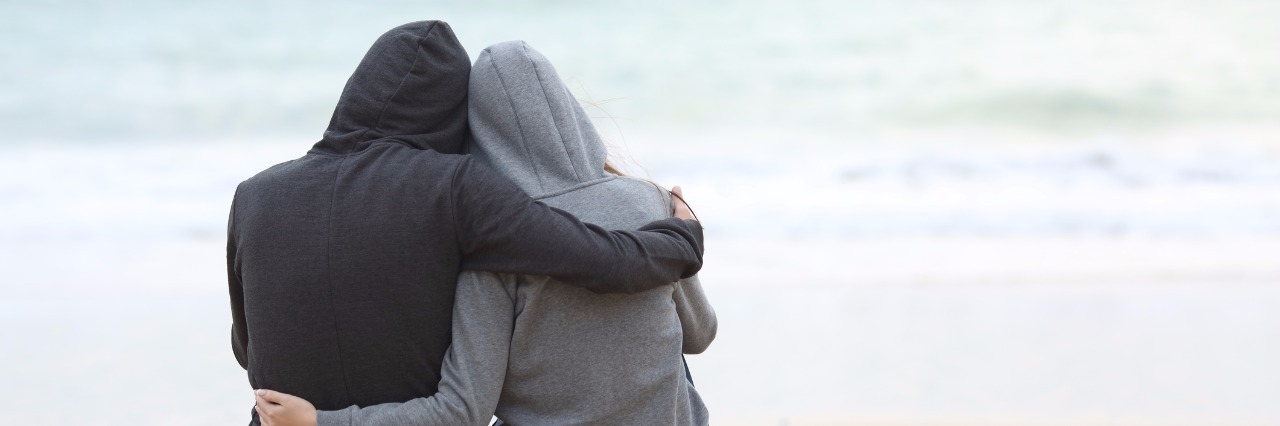 Maintaining Relationships With Chronically Ill Loved Ones two people wearing sweatshirts and hugging on the beach