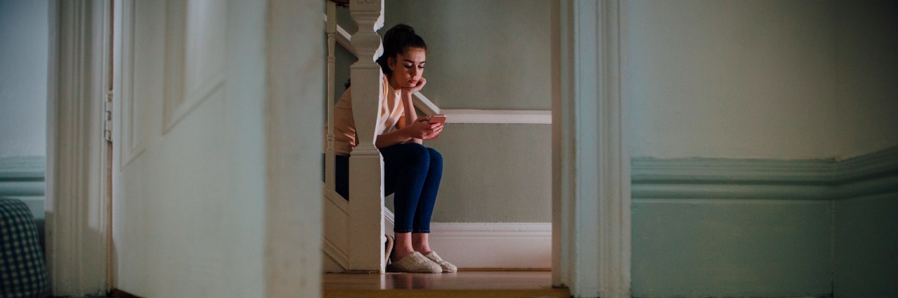 Getting Back Up After Depression Knocked Me Down Teenage girl sitting at the bottom of a staircase using a smartphone.