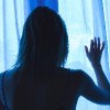 Lonesome girl holding a curtain at night looking out window