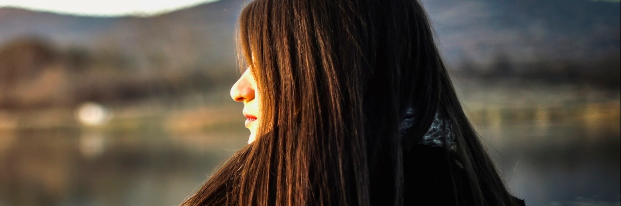 Profile of woman looking at landscape with mountains and a lake or river in the background