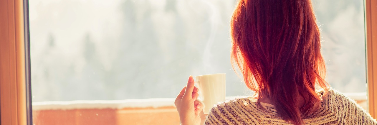 What 'Quality of Life' Means in My Life With Cancer Woman sitting in a comfortable chair drinking coffee and looking through window at snow covered mountain.