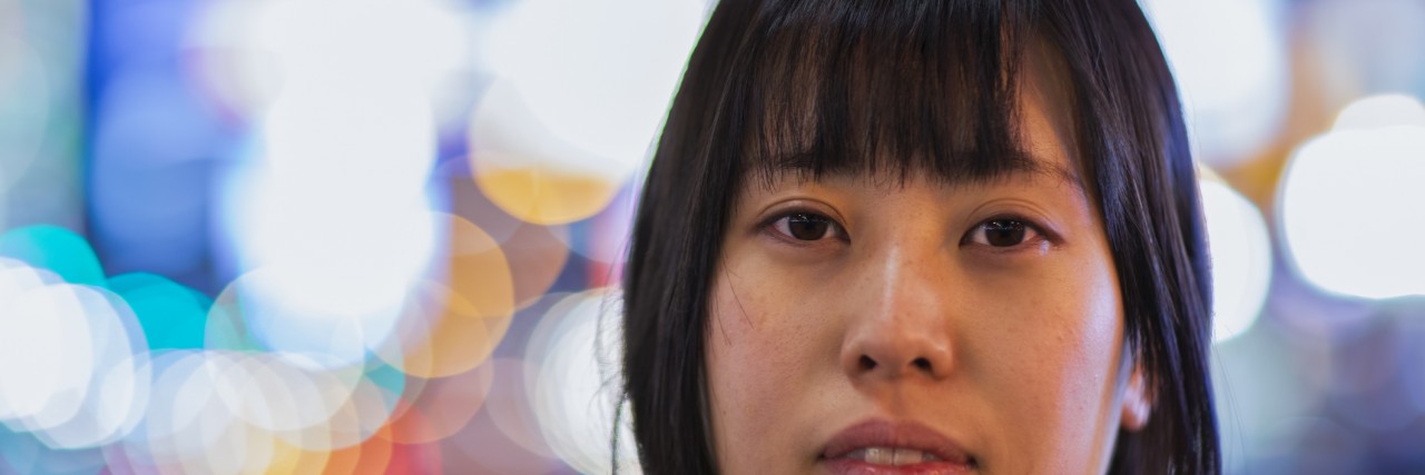 What I Wish My Teen Self Had Realized About Self-Harm and Depression A portrait of a Japanese girl is taken at night with beautiful lights in the background while she is looking into the camera.